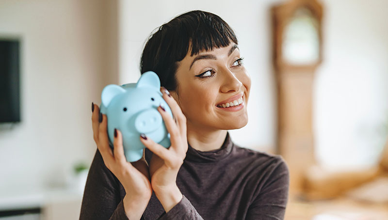 Una donna sorridente che tiene in mano un salvadanaio a forma di maialino azzurro, pensando a come risparmiare tasse con Previdenza Cooperativa.