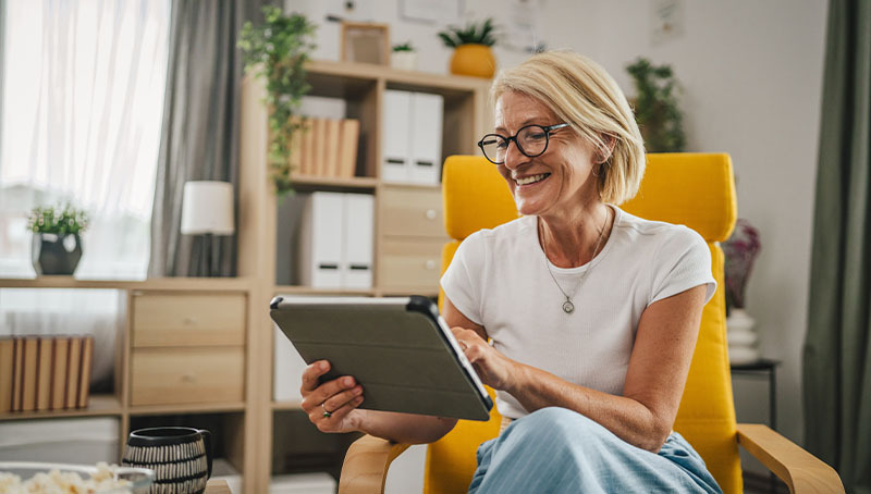 Una donna anziana felice usa un tablet per consultare un glossario della previdenza in un ambiente domestico accogliente.