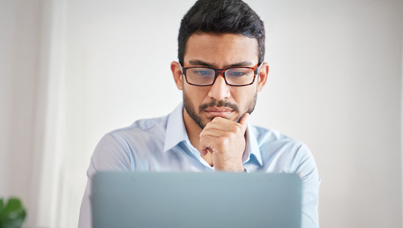 Un giovane professionista con gli occhiali osserva con attenzione lo schermo di un laptop, simboleggiando il controllo dei versamenti al fondo Previdenza Cooperativa nella propria busta paga.