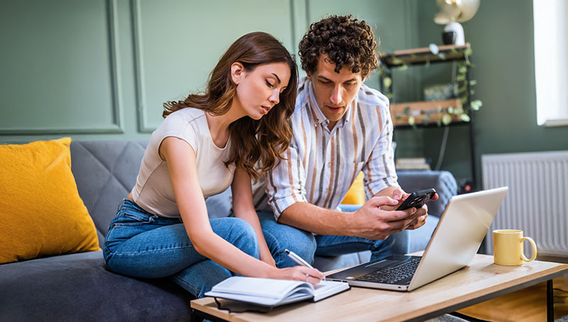 Una coppia analizza i costi e i vantaggi di aderire a Previdenza Cooperativa utilizzando un laptop e uno smartphone in casa