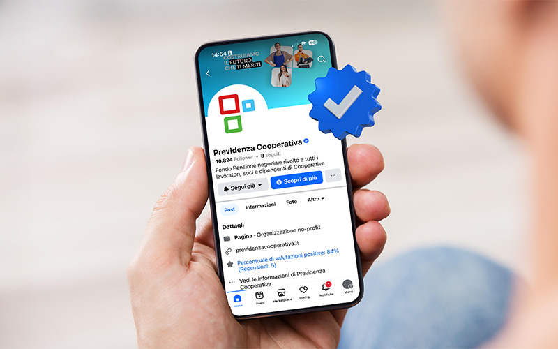 Mano che tiene uno smartphone con la Pagina Facebook di Previdenza Cooperativa aperta e il badge di verifica blu in evidenza sullo schermo.