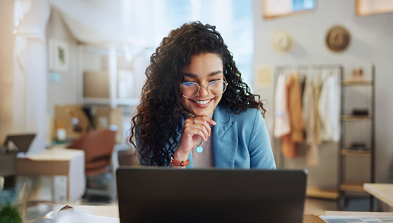 Giovane professionista sorridente che lavora al computer in un ufficio creativo, simbolo di pianificazione finanziaria per il futuro.
