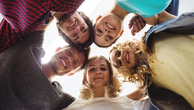 Gruppo di giovani adulti sorridenti in cerchio guarda verso il basso, immagine sul tema delle nuove regole per i fondi pensione negoziali