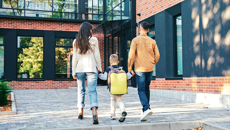 Genitori accompagnano il figlio con lo zaino verso un edificio, immagine sul tema del futuro e della previdenza per i figli